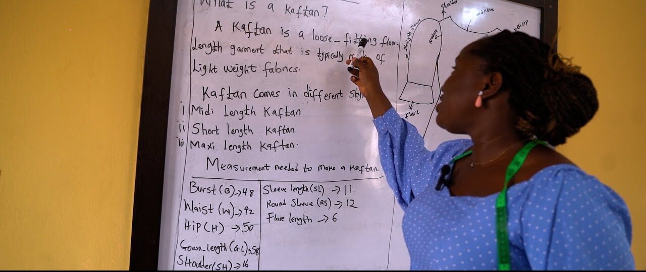 A fashion instructor explaining kaftan measurements on a whiteboard